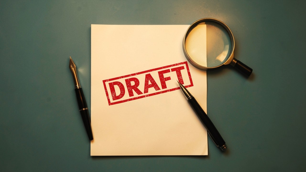 A legal document with a pen and a magnifying glass, the document showing a red 'DRAFT' stamp (no other text).